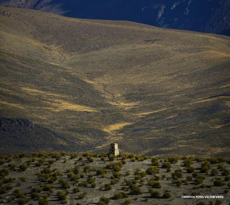Un campo montañoso de colores verdes y amarillos con una pequeña edificación en el centro